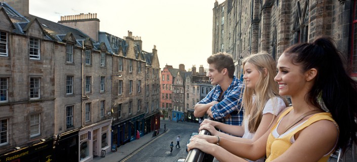Grassmarket, a historic street in Edinburgh. Three young people on the terrace overlooking the street and terraced houses.